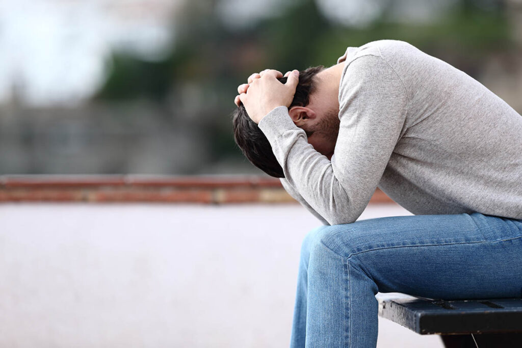 distraught young man sitting outside with head in his hands attempting to understand the opioid epidemic statistcis