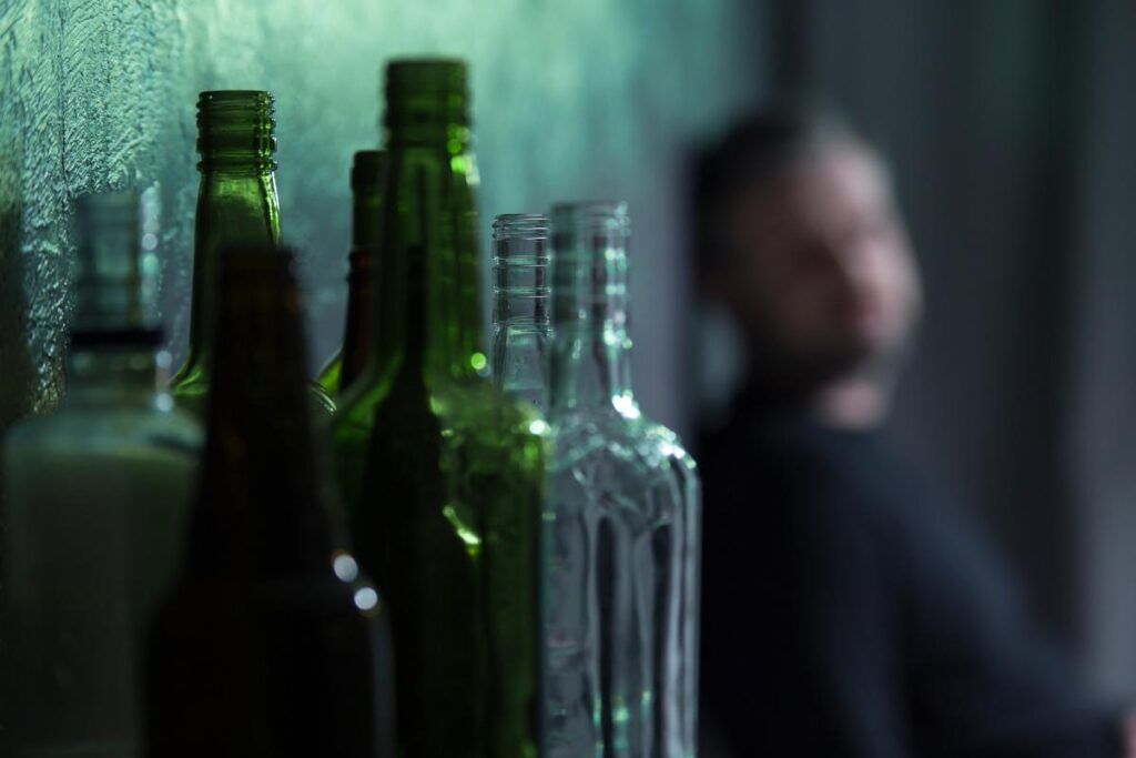 a blurry man stares intensely at alcohol bottles that are in focus