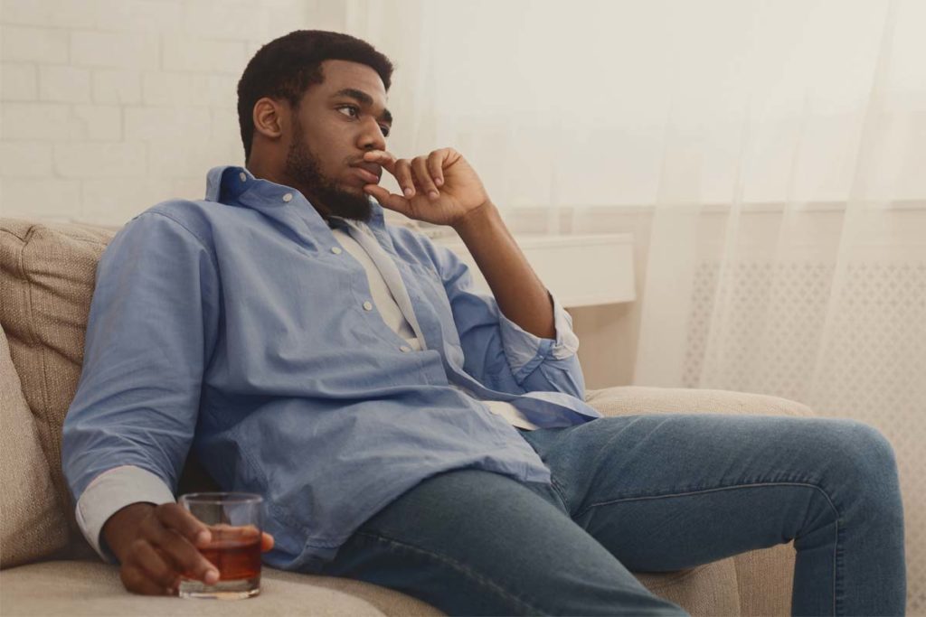 alcohol and depression, man sitting on couch with drink in hand