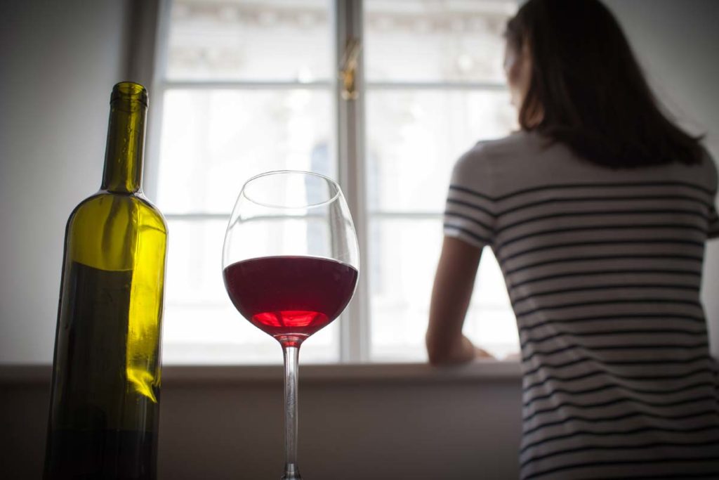 am i an alcoholic, person looking out window with glass of wine and bottle in foreground