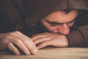substance use disorder, man in hoodie with face in arms on table