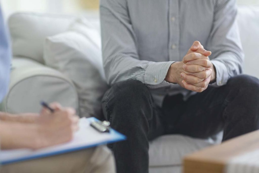 what is dual diagnosis, patient with hands folded on couch as therapist writes on chart