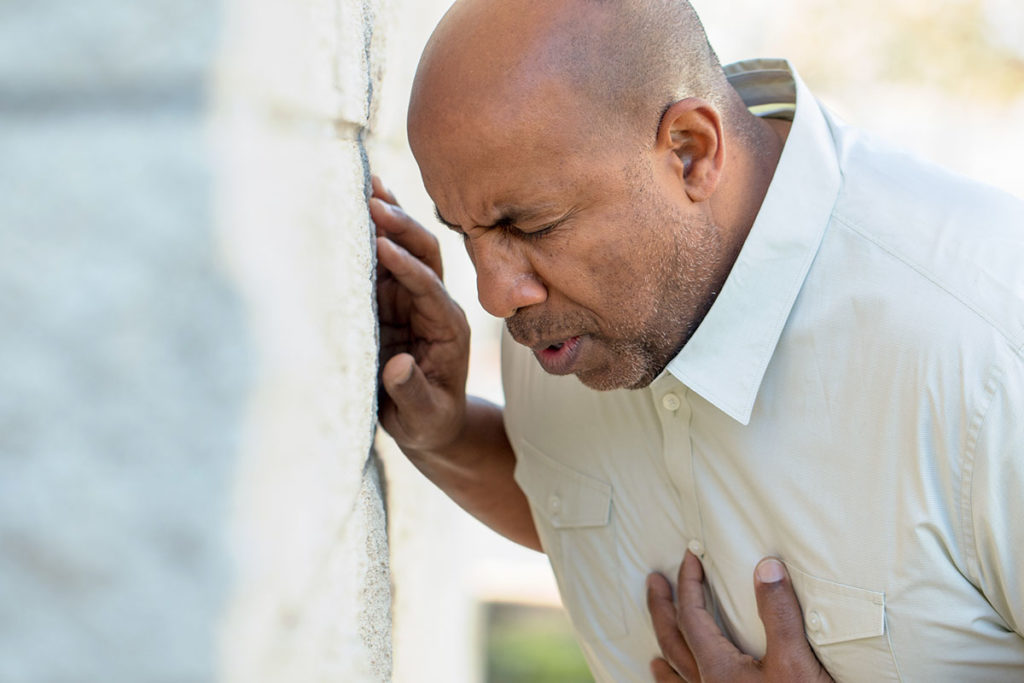 man leaning against wall clutching chest showing Signs of An Anxiety Attack